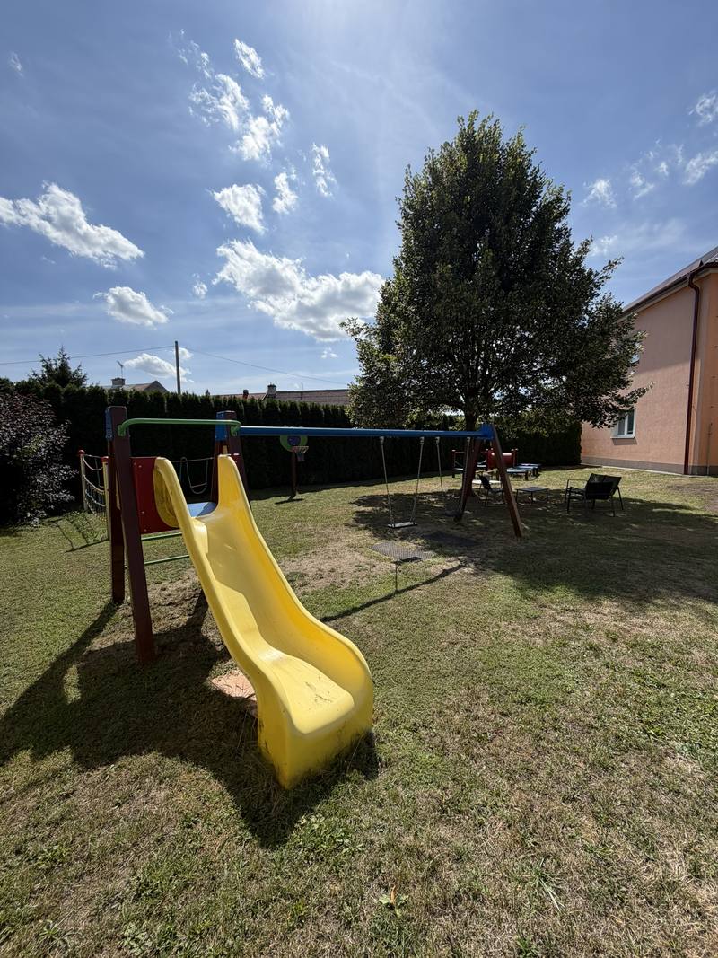 Žlutá skluzavka a houpačky na travnaté zahradě školky